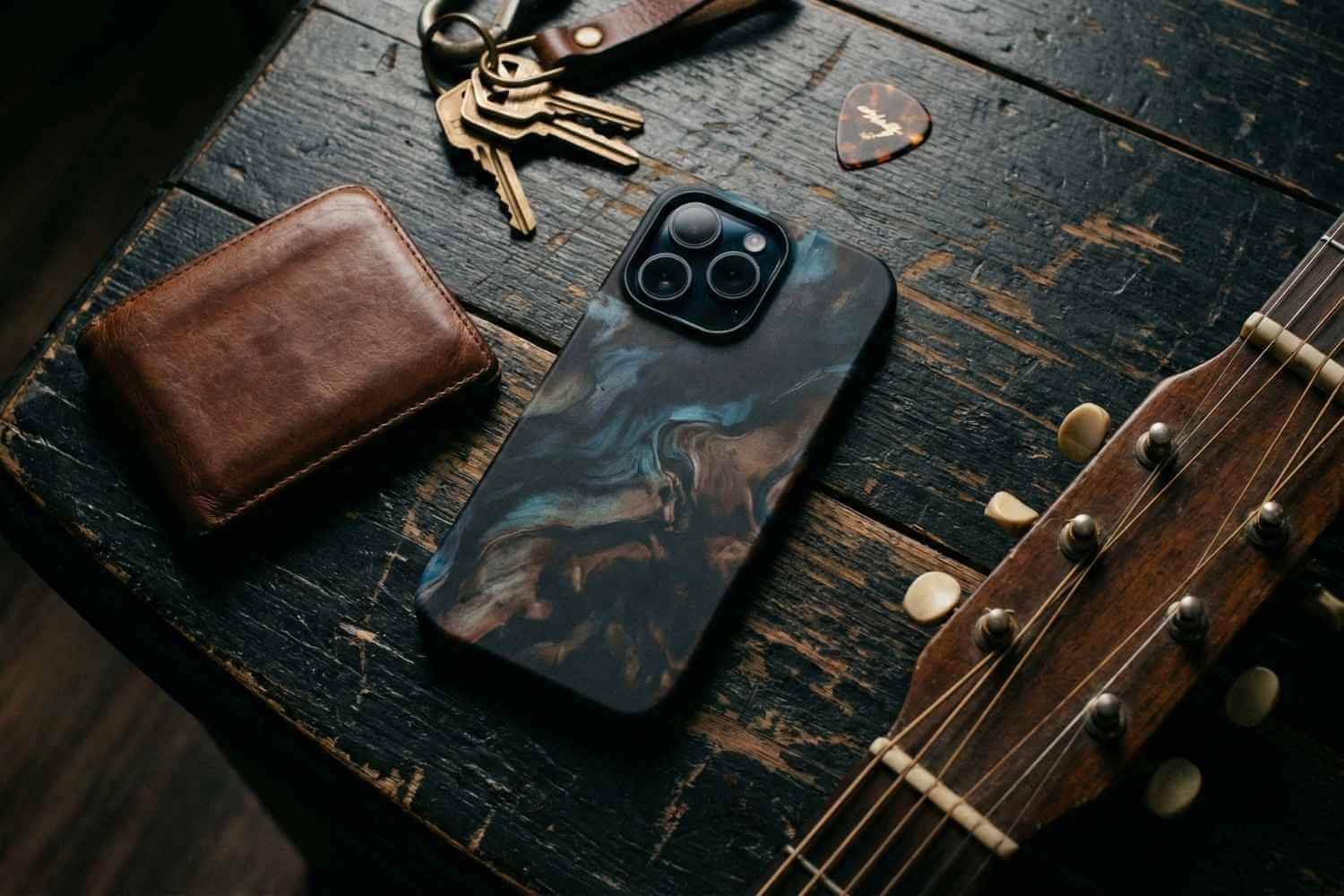 Musician everyday carry essentials including tough phone case and guitar picks on a wooden table.